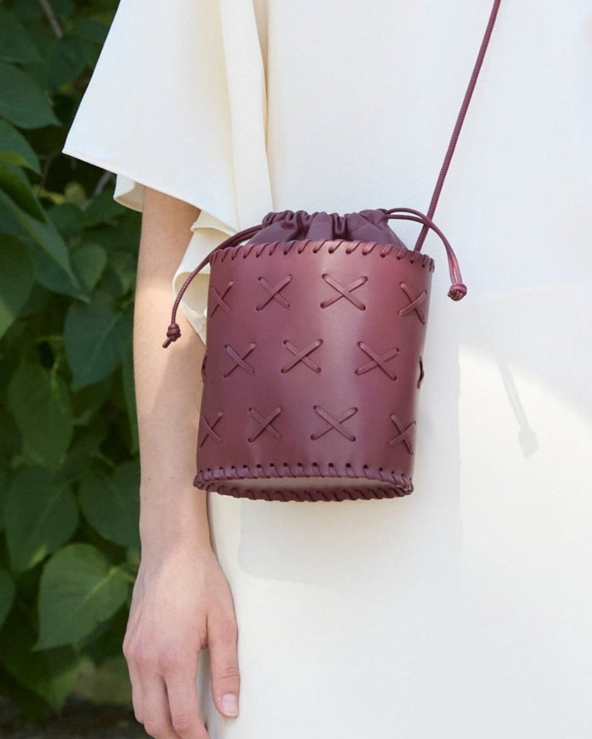 Burgundy leather drawstring bag held by a person with a blurred green background