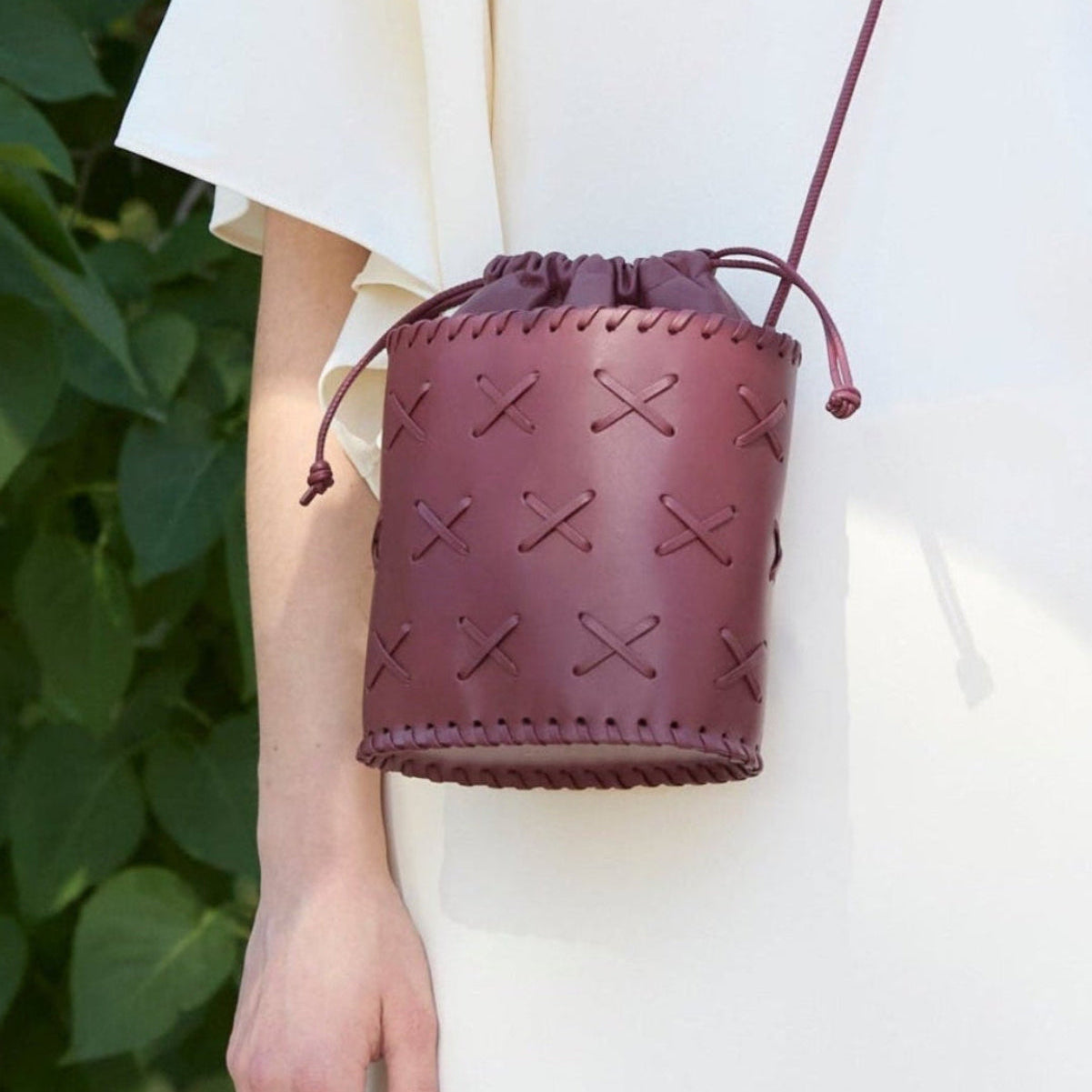 Burgundy leather drawstring bag held by a person with a blurred green background