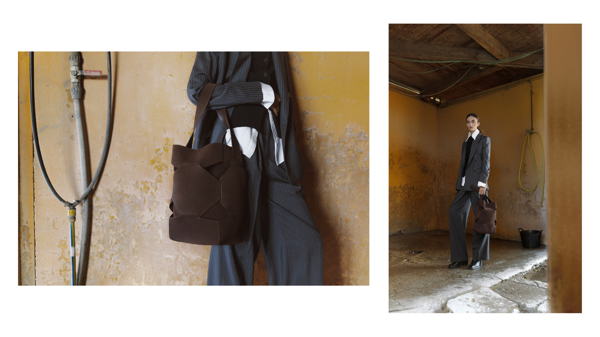 A fashion editorial collage showing a model in a dark charcoal suit and white shirt carrying a dark brown geometric structured tote bag, set against a rustic yellow wall on the left and in a dimly lit industrial room on the right.